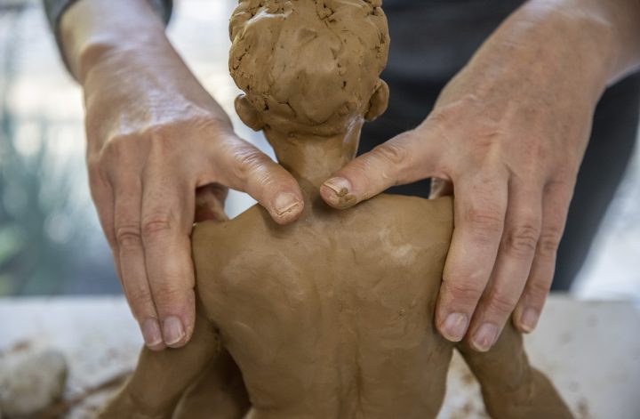 Persoon boetseert een menselijk figuur in klei